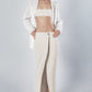 Woman wearing a beige linen cotton bra crop top with matching low-waist maxi skirt and white shirt