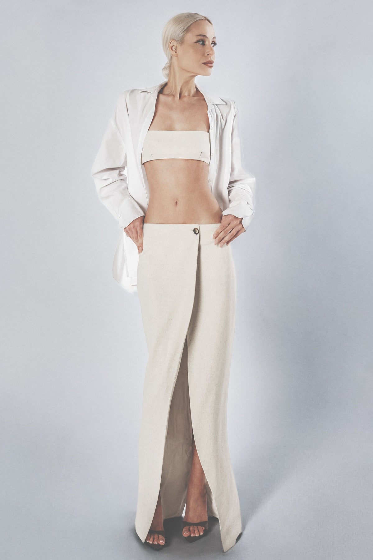 Woman wearing a beige linen cotton bra crop top with matching low-waist maxi skirt and white shirt